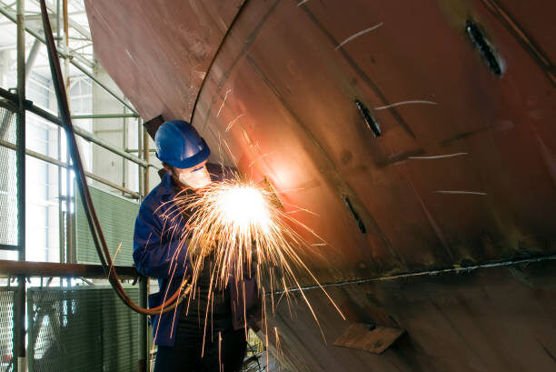 Welding new steel plates on a ship's hull during repair work on a ship in a dry dock.